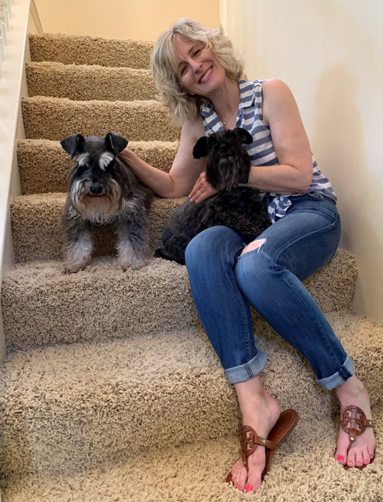 A woman seating in a home stairs with her two dogs.